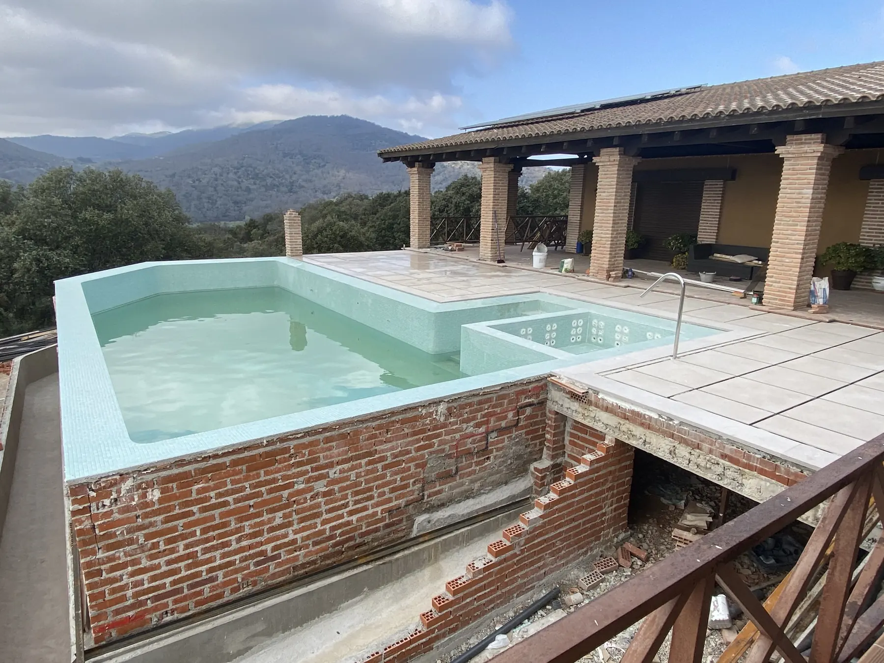 Piscina de la finca terminada y llena, con la playa de piedra y la sierra al fondo