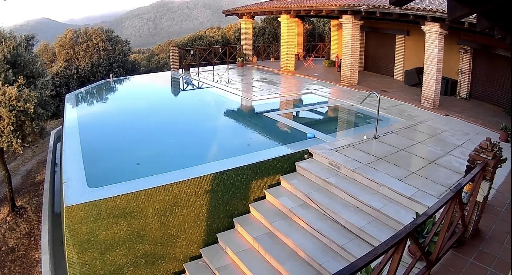 Piscina desbordante con gresite verde en una finca de la sierra al amanecer